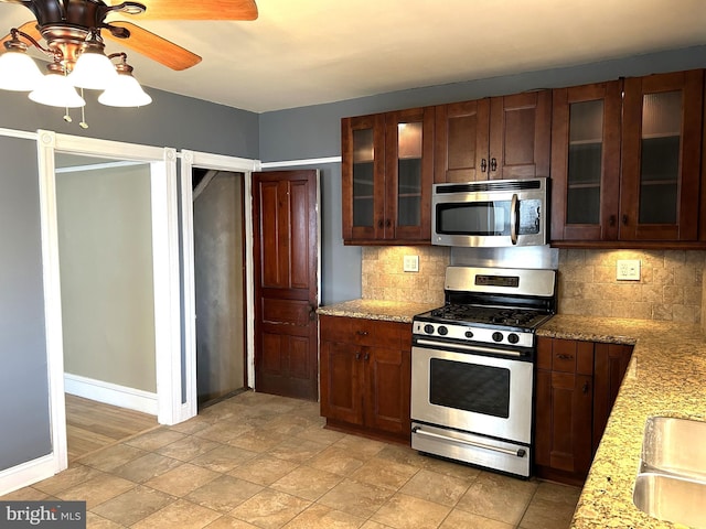 kitchen featuring light stone counters, decorative backsplash, stainless steel appliances, and ceiling fan