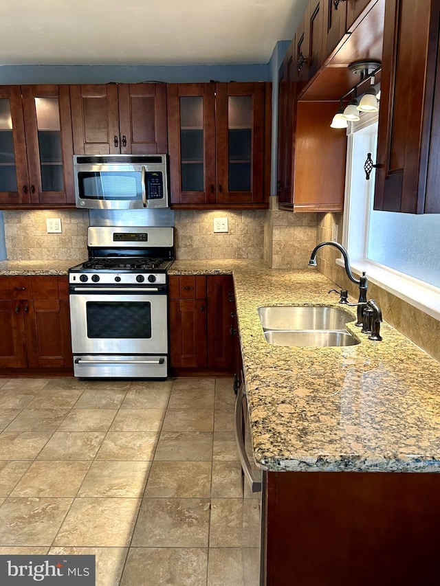 kitchen featuring stainless steel appliances, sink, light stone counters, and decorative backsplash