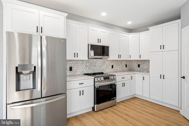 kitchen with tasteful backsplash, white cabinetry, light hardwood / wood-style floors, stainless steel appliances, and light stone countertops