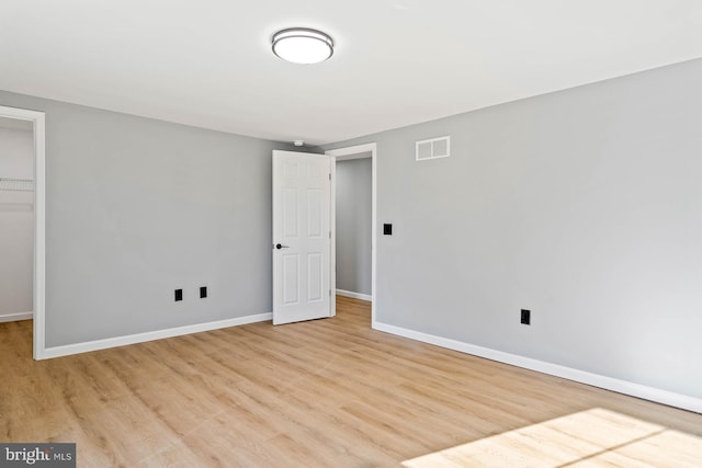 unfurnished bedroom featuring a walk in closet, a closet, and light wood-type flooring