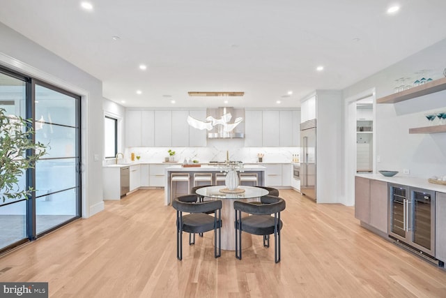 kitchen with wall chimney range hood, stainless steel appliances, a center island, white cabinets, and beverage cooler