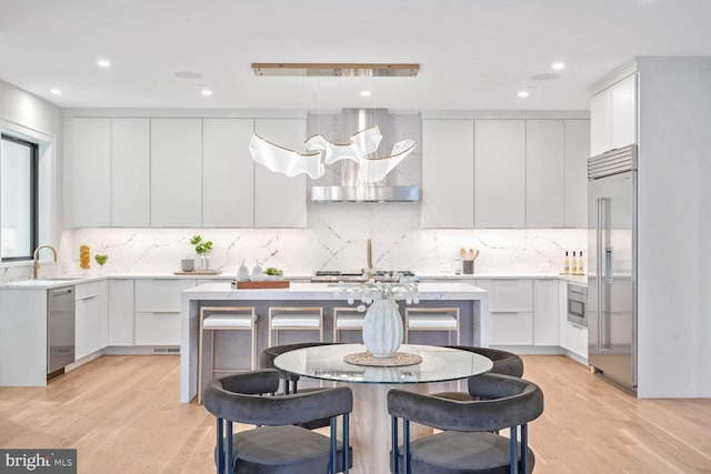 kitchen with wall chimney range hood, sink, white cabinetry, stainless steel appliances, and a center island