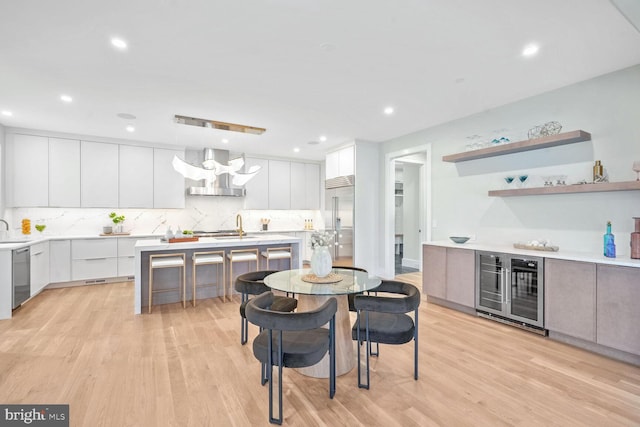 kitchen with wine cooler, white cabinetry, hanging light fixtures, stainless steel appliances, and wall chimney range hood