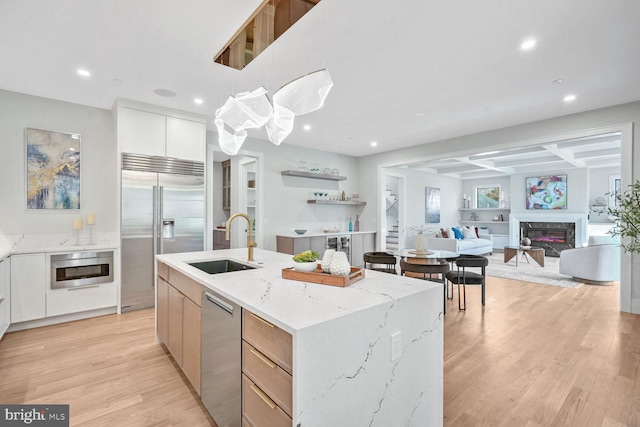 kitchen with sink, appliances with stainless steel finishes, a kitchen island with sink, light stone countertops, and white cabinets