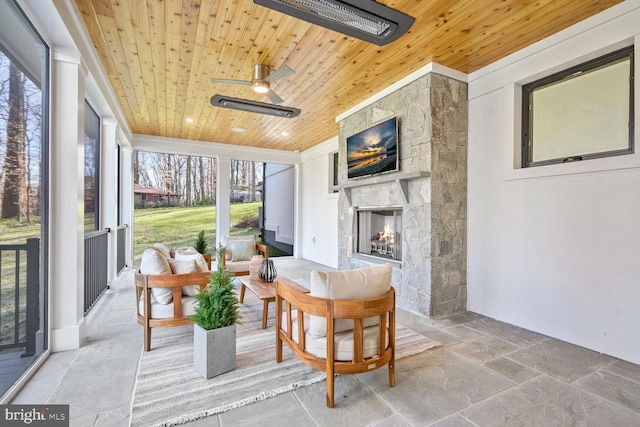 sunroom with ceiling fan, wooden ceiling, and an outdoor stone fireplace