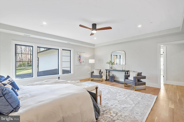 bedroom featuring ceiling fan, a tray ceiling, and light hardwood / wood-style floors