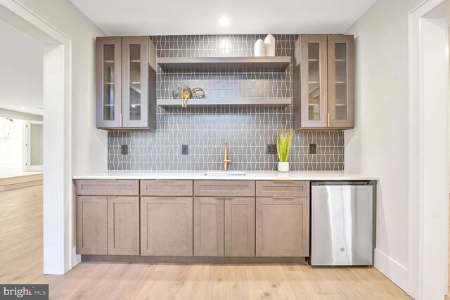 bar featuring tasteful backsplash, fridge, sink, and light wood-type flooring