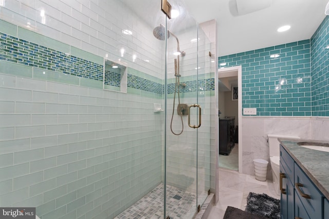 bathroom featuring vanity, toilet, a shower with door, and tile walls