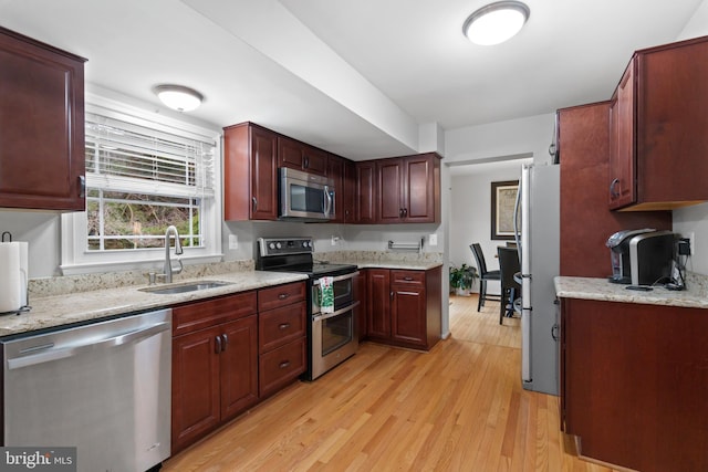 kitchen featuring appliances with stainless steel finishes, light stone countertops, sink, and light hardwood / wood-style flooring