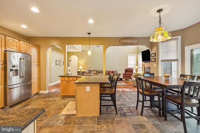 kitchen with stainless steel refrigerator with ice dispenser, sink, hanging light fixtures, light brown cabinets, and a kitchen island