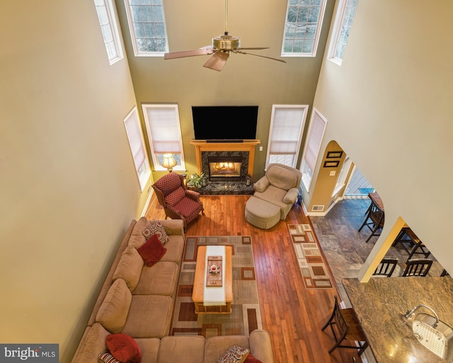 living room featuring ceiling fan, a towering ceiling, wood-type flooring, and a fireplace