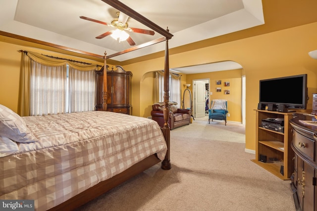 bedroom featuring a raised ceiling, light carpet, and ceiling fan