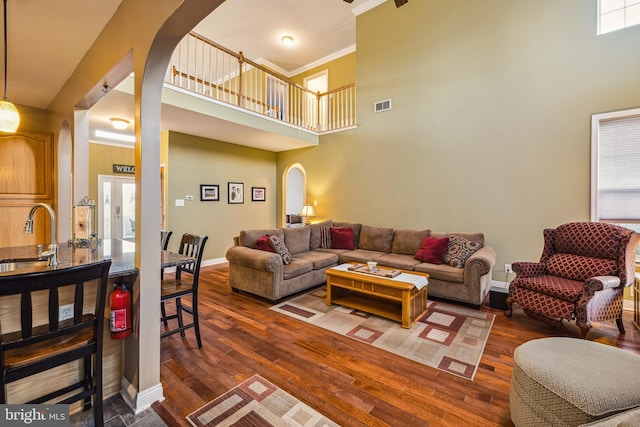 living room with a high ceiling, crown molding, sink, and dark wood-type flooring