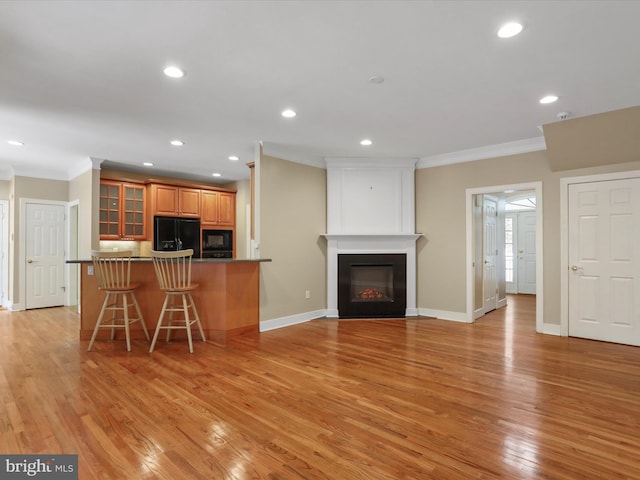 kitchen with a breakfast bar, a fireplace, black appliances, crown molding, and light wood-type flooring