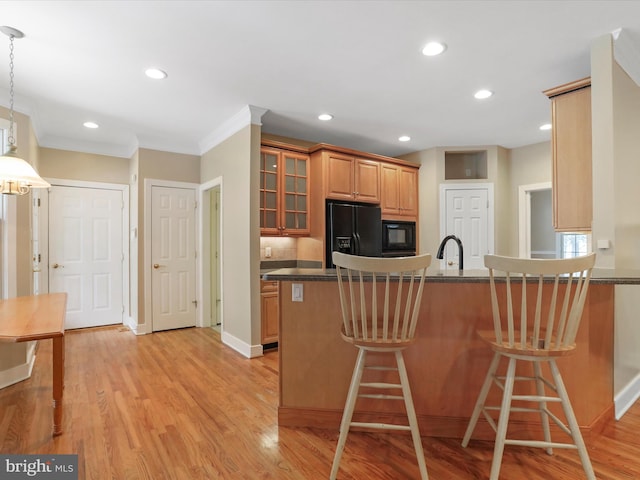 kitchen featuring light hardwood / wood-style flooring, a kitchen breakfast bar, kitchen peninsula, pendant lighting, and black appliances