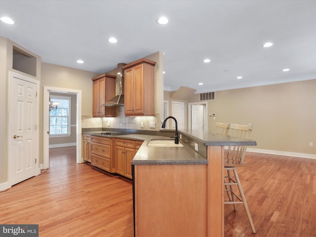 kitchen with sink, wall chimney range hood, black electric stovetop, a kitchen bar, and kitchen peninsula