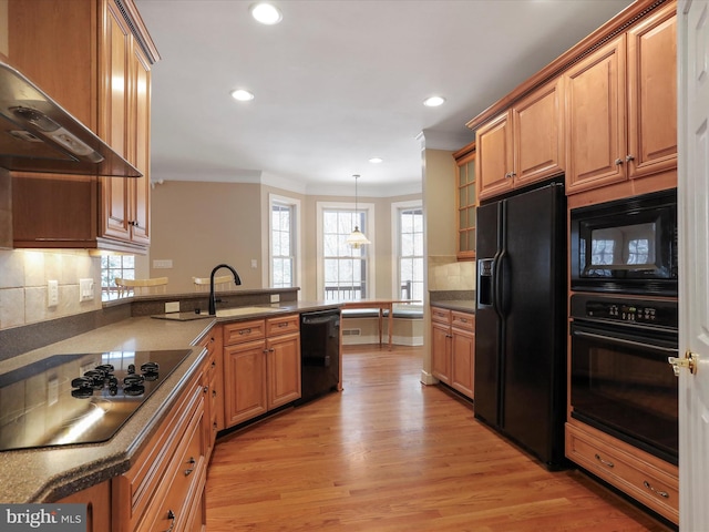 kitchen with backsplash, hanging light fixtures, black appliances, wall chimney range hood, and light wood-type flooring