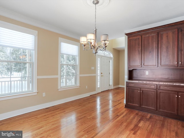 unfurnished dining area featuring ornamental molding, a healthy amount of sunlight, an inviting chandelier, and light wood-type flooring