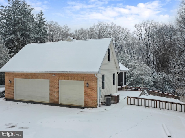 snow covered property featuring a garage and central AC unit