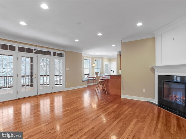 unfurnished living room with french doors, ornamental molding, and light wood-type flooring