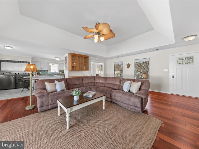 living room featuring wood-type flooring, ceiling fan, and a tray ceiling