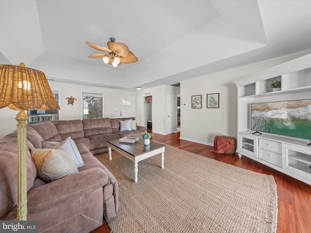 living room featuring dark hardwood / wood-style flooring, a tray ceiling, and ceiling fan