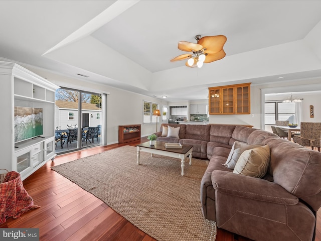 living room featuring hardwood / wood-style floors, ceiling fan with notable chandelier, a wealth of natural light, and a raised ceiling