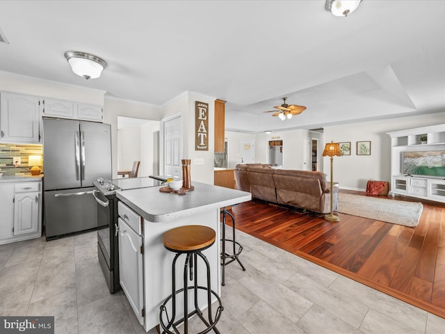 kitchen featuring a kitchen bar, tasteful backsplash, ornamental molding, stainless steel appliances, and white cabinets