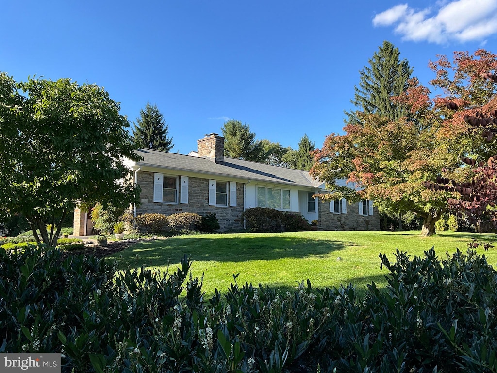 ranch-style home with stone siding, a chimney, and a front yard