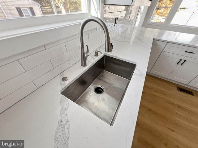 interior details with white cabinetry, wood-type flooring, sink, backsplash, and light stone countertops