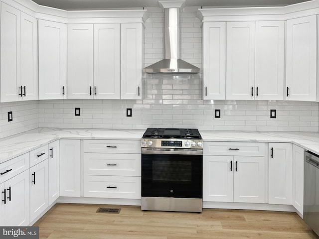 kitchen with white cabinetry, stainless steel appliances, light stone countertops, light hardwood / wood-style floors, and wall chimney exhaust hood