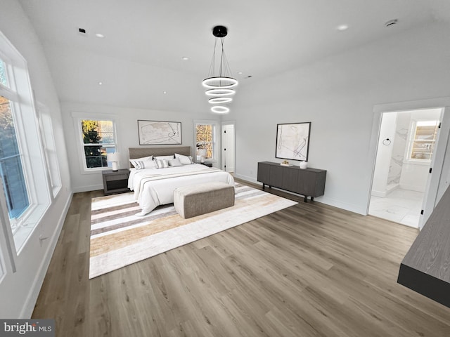 unfurnished bedroom featuring ensuite bathroom, high vaulted ceiling, an inviting chandelier, and light hardwood / wood-style flooring