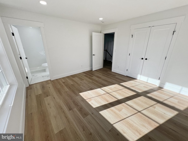 unfurnished bedroom featuring connected bathroom, wood-type flooring, and a closet