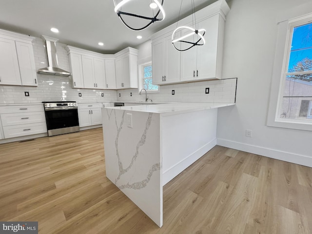 kitchen with wall chimney exhaust hood, stainless steel electric range oven, hanging light fixtures, decorative backsplash, and white cabinets