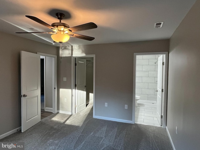 unfurnished bedroom with ceiling fan, ensuite bath, a spacious closet, and dark colored carpet