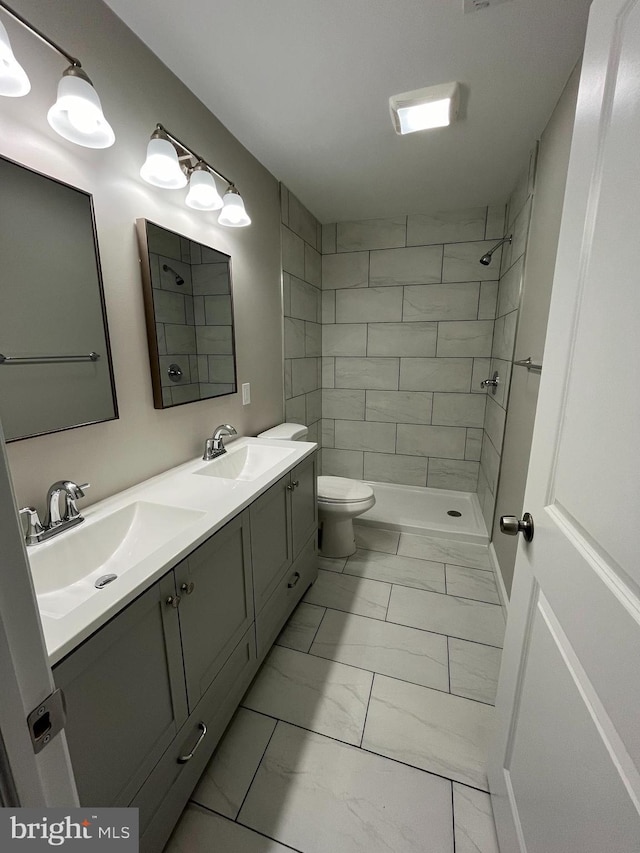 bathroom featuring vanity, a tile shower, and toilet