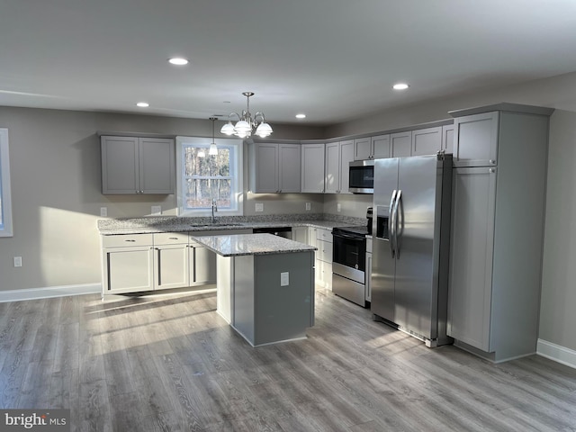 kitchen with a kitchen island, appliances with stainless steel finishes, light stone counters, hanging light fixtures, and a sink