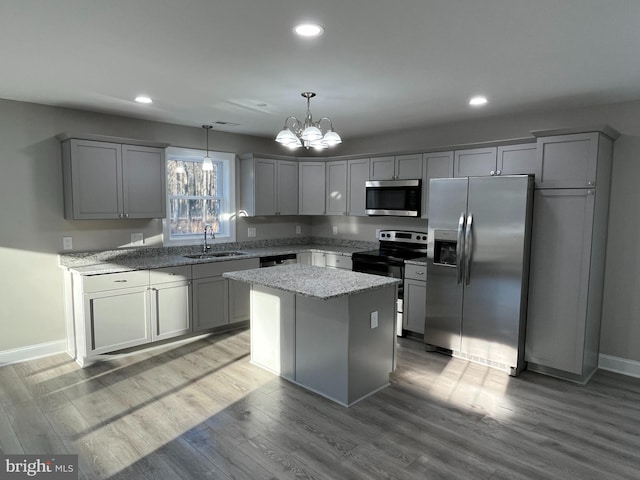 kitchen with sink, appliances with stainless steel finishes, hanging light fixtures, a center island, and light stone countertops