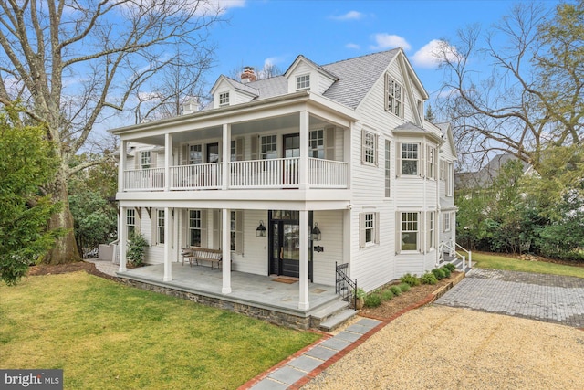 view of front of home with a porch, a balcony, a chimney, and a front lawn