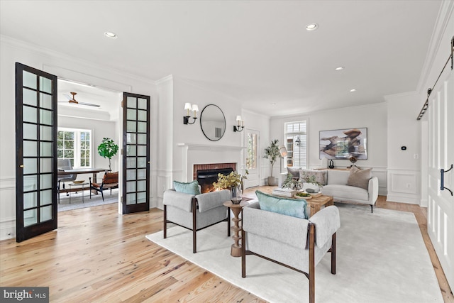 living room featuring light wood finished floors, ornamental molding, french doors, a decorative wall, and a brick fireplace