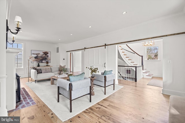 living room with light wood finished floors, ornamental molding, stairs, a barn door, and a wealth of natural light