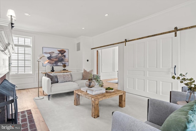 living room featuring visible vents, a wainscoted wall, a barn door, hardwood / wood-style floors, and ornamental molding