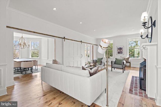 living room with a fireplace, light wood-type flooring, a barn door, and crown molding