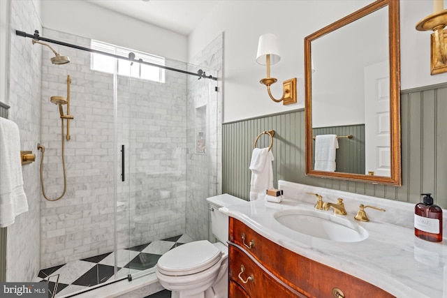 bathroom featuring vanity, a shower stall, toilet, and a wainscoted wall