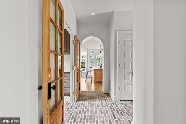 hallway featuring arched walkways, recessed lighting, and brick floor