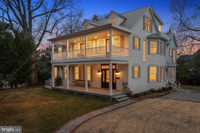 back of property at dusk featuring a balcony, a yard, and a chimney