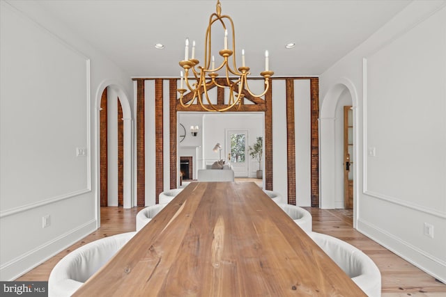 dining space featuring recessed lighting, arched walkways, an inviting chandelier, light wood finished floors, and a brick fireplace