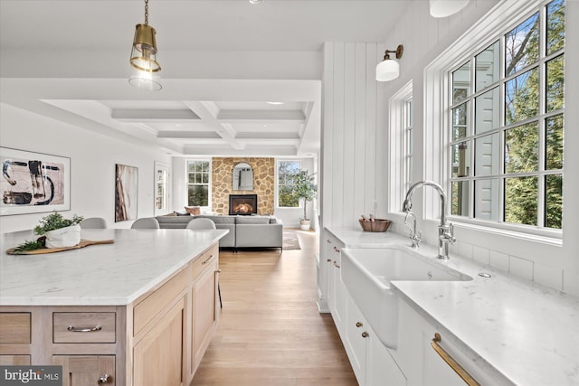 kitchen featuring light wood finished floors, coffered ceiling, a sink, beamed ceiling, and a wealth of natural light