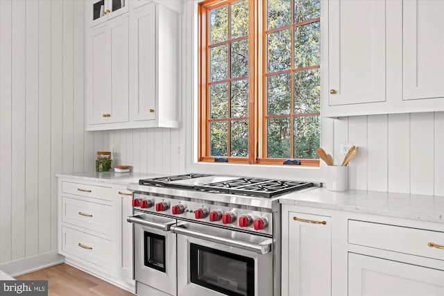 kitchen with light wood-type flooring, white cabinetry, range with two ovens, glass insert cabinets, and light stone countertops