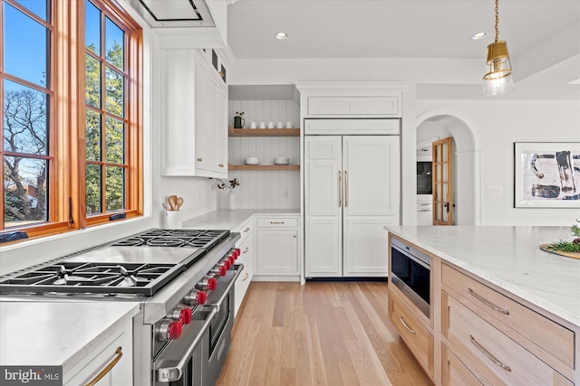 kitchen with open shelves, arched walkways, light wood-style floors, built in appliances, and white cabinetry